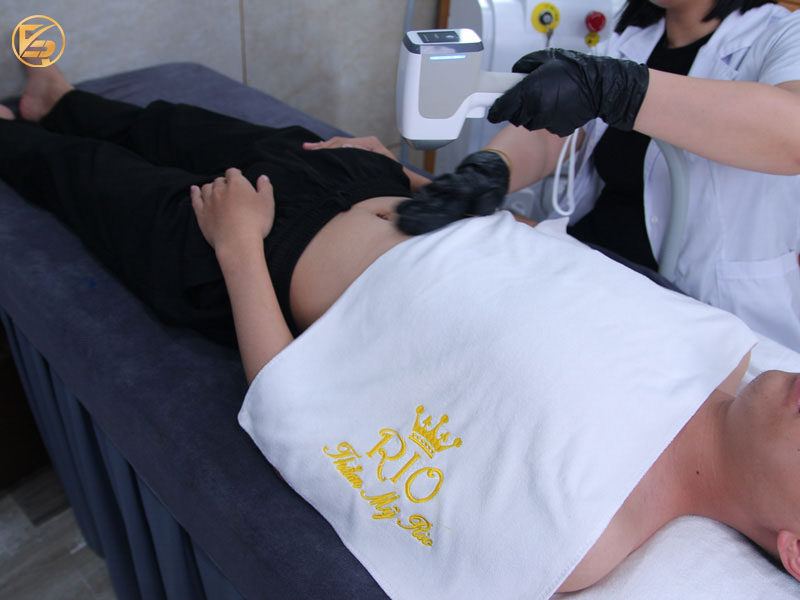Kỹ thuật viên đeo găng tay đen đang sử dụng máy công nghệ cao điều trị da vùng bụng cho khách hàng tại Thẩm mỹ Rio