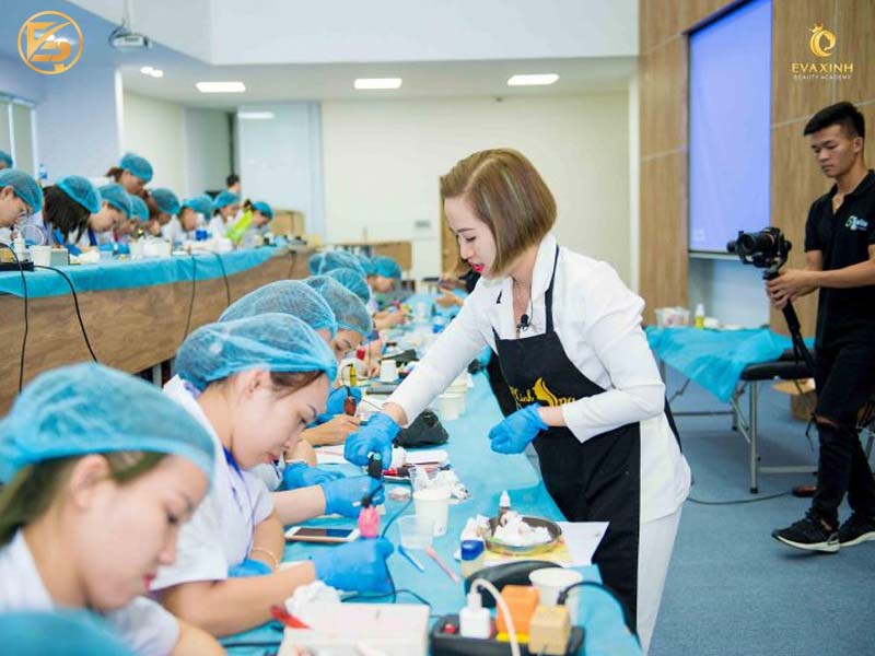 Giảng viên Eva Xinh Beauty Academy cầm tay chỉ việc hướng dẫn học viên thực hành kỹ thuật phun xăm thẩm mỹ trong lớp học chuyên nghiệp.