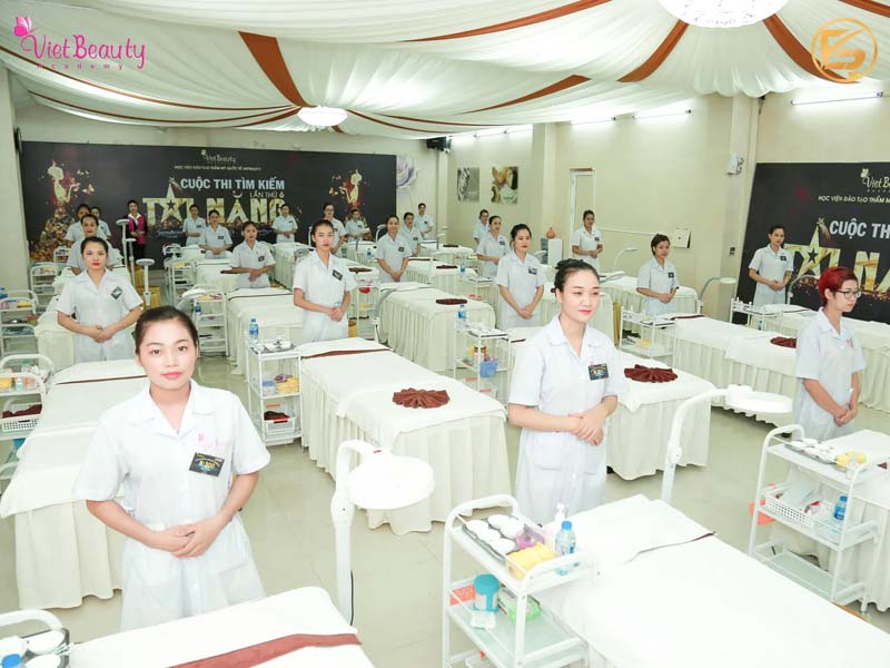 Các thí sinh mặc áo blouse trắng đứng trang nghiêm bên giường thực hành tại Cuộc thi tìm kiếm tài năng VietBeauty Academy.