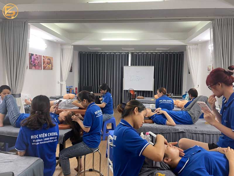 Học viên tại Học viện Chihun mặc đồng phục xanh đang thực hành các kỹ thuật chăm sóc da và massage trên người mẫu trong lớp học